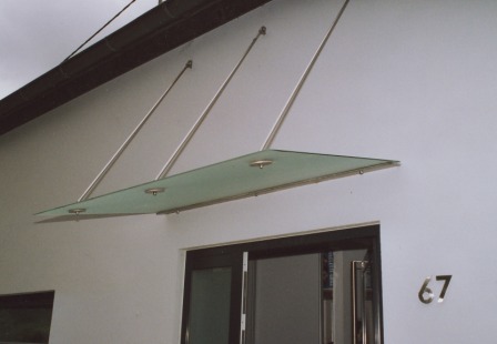 Vordach in Glas mit einer diagonalen Abhängung in Edelstahl